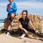 A couple stretching and using a phone on a scenic beach in Portugal.